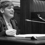 This is a picture of Ms Vincent in the South Australian Legislative Council. The image has been photographed in black and white. She is using a manual wheelchair and sitting at a desk, speaking into a small microphone.